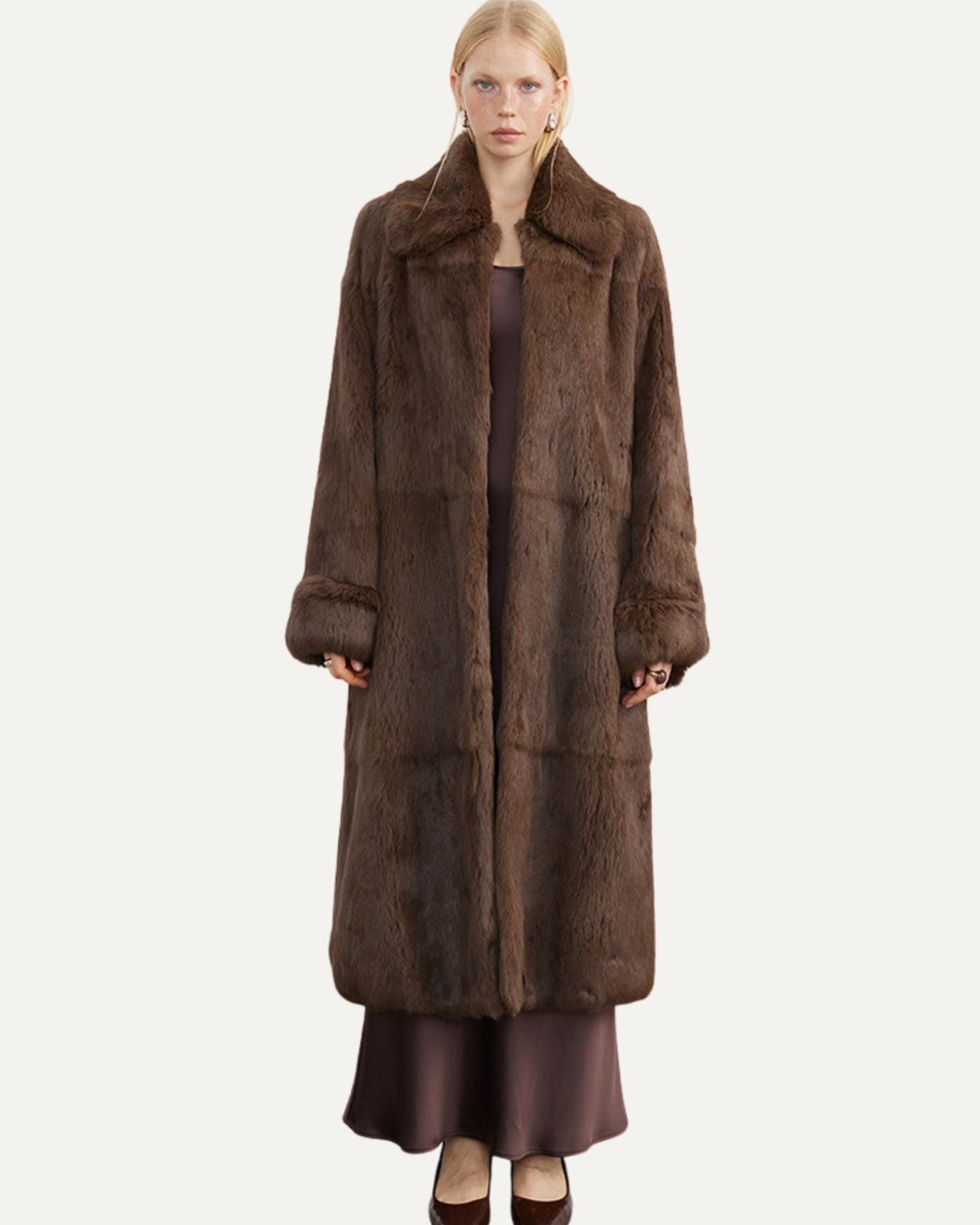 Woman in camel coat and cream luggage, contemporary transit setting, quiet luxury travel ready