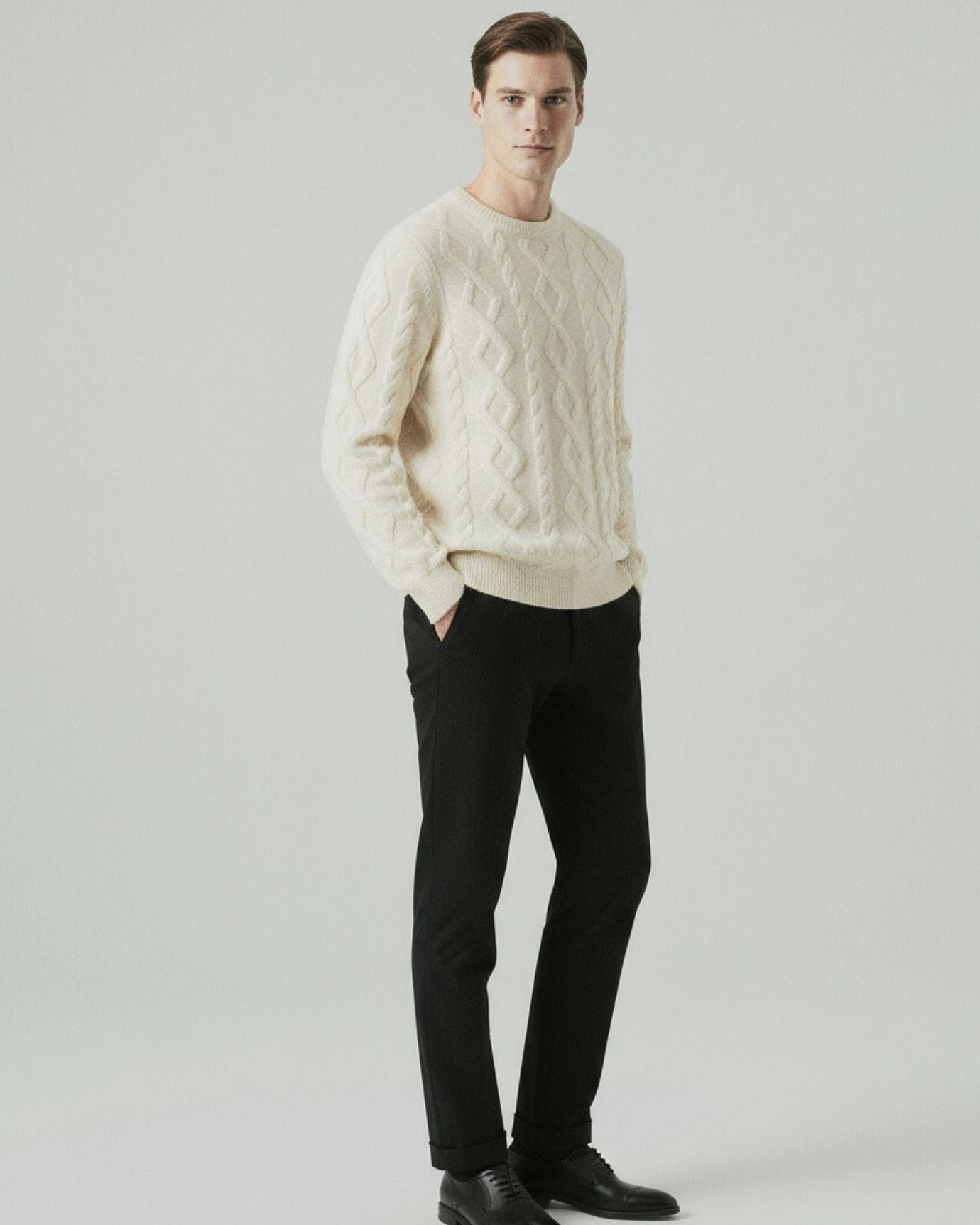 Man wearing a cream sweater and black pants on a plain background