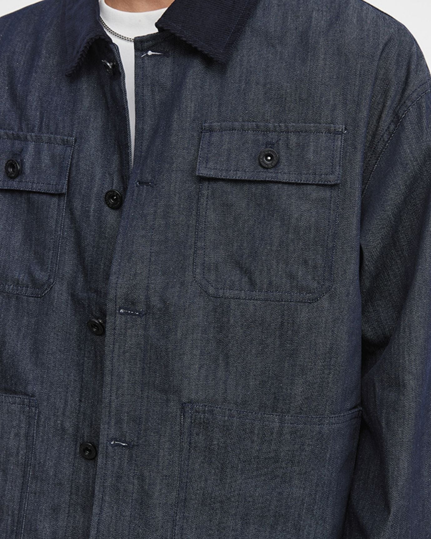 Close-up of a dark denim jacket with button details on a white background