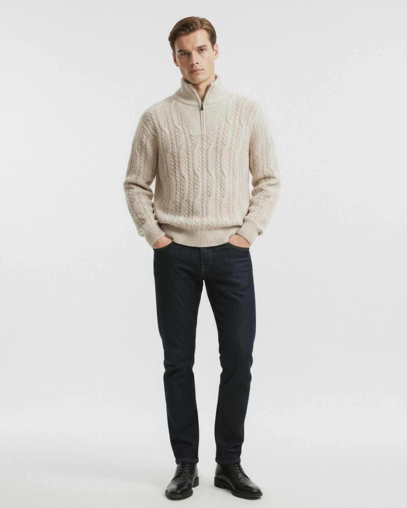 Man wearing a beige cable knit sweater and dark jeans on a white background
