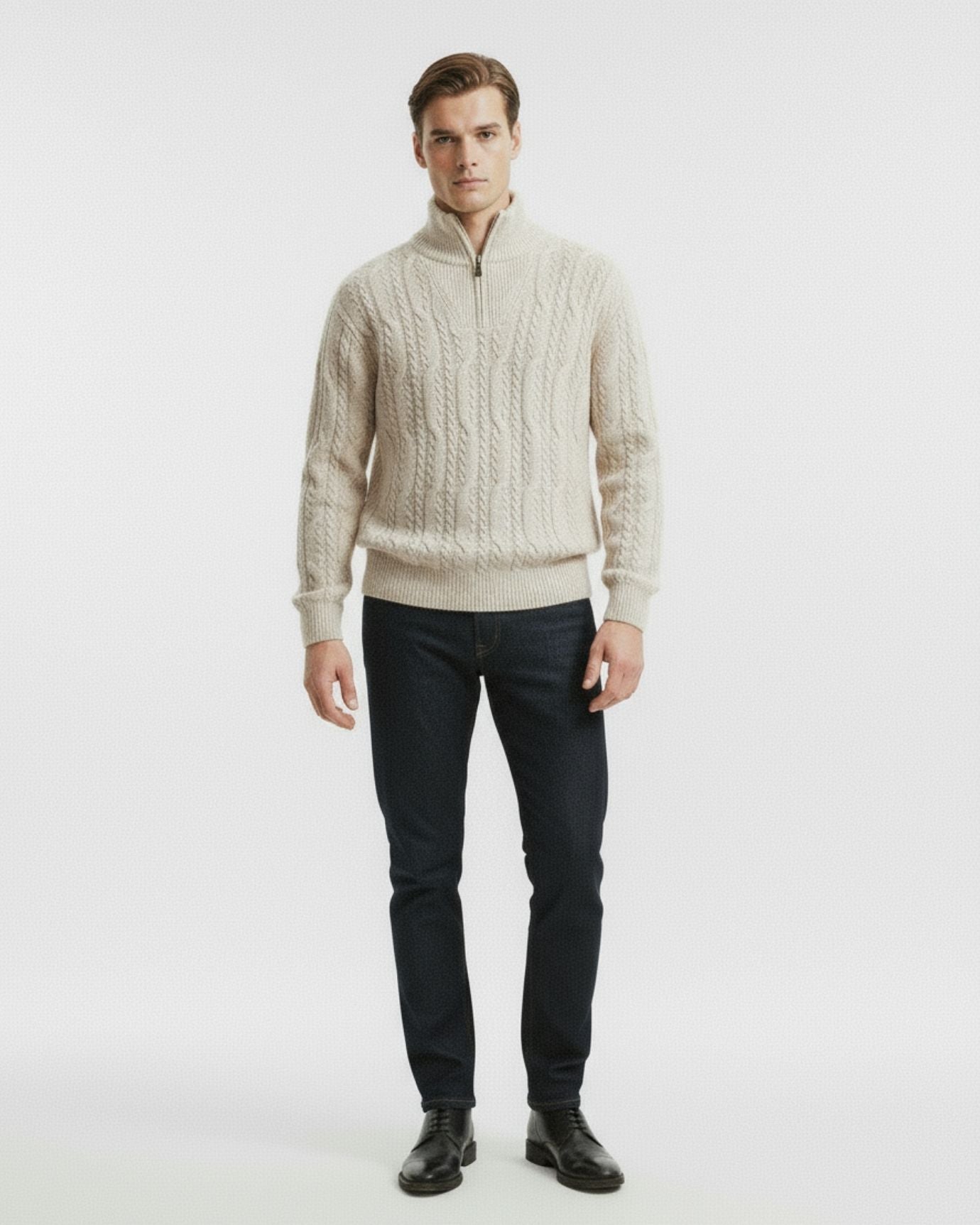 Man wearing a beige cable knit sweater and dark jeans on a white background