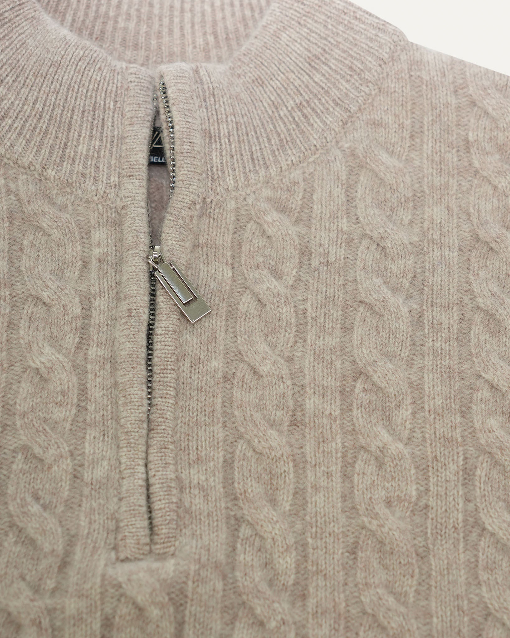 Close-up of a cable knit sweater with a zipper detail on a plain background