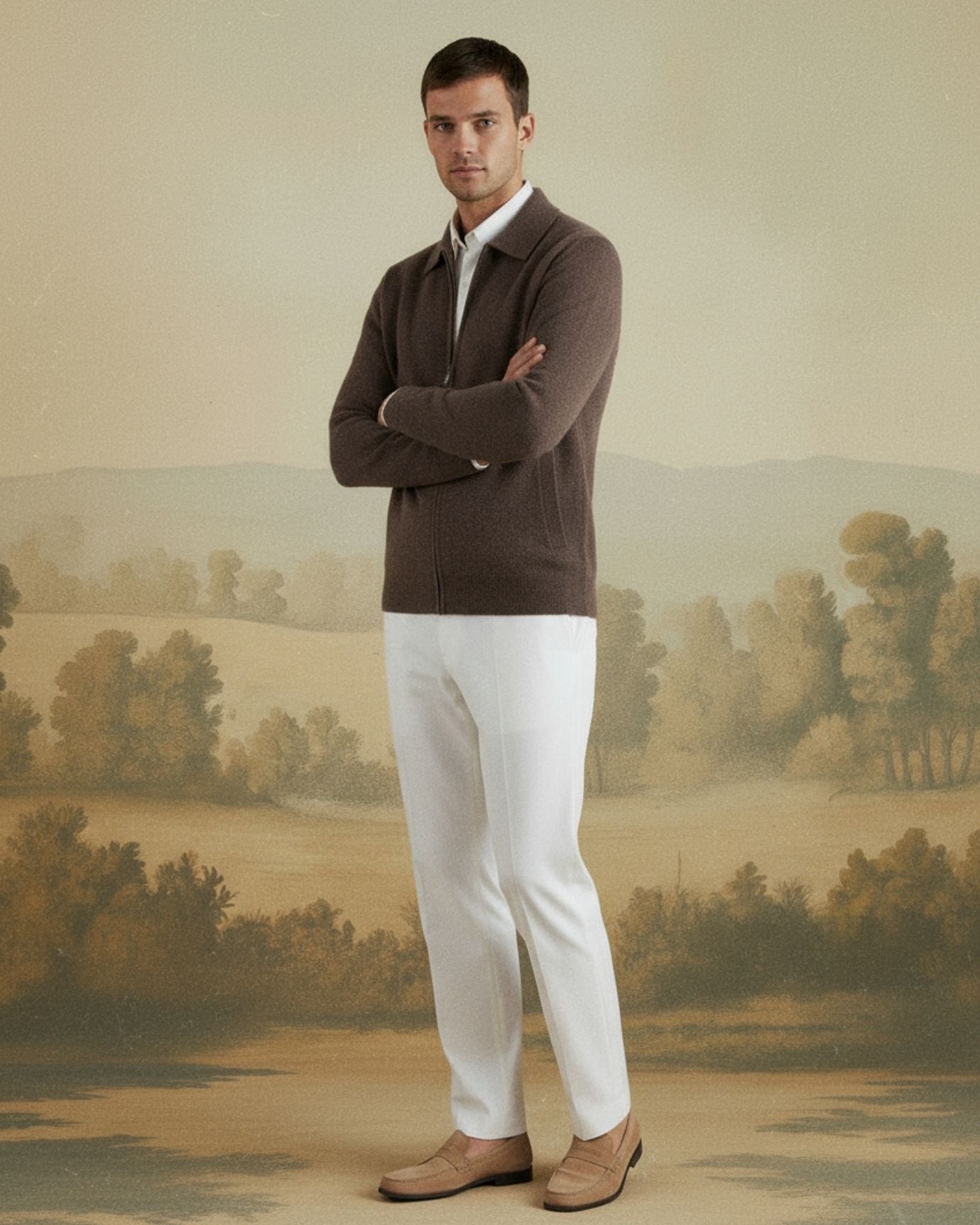Man wearing a brown sweater and white pants standing in front of a scenic wall mural.