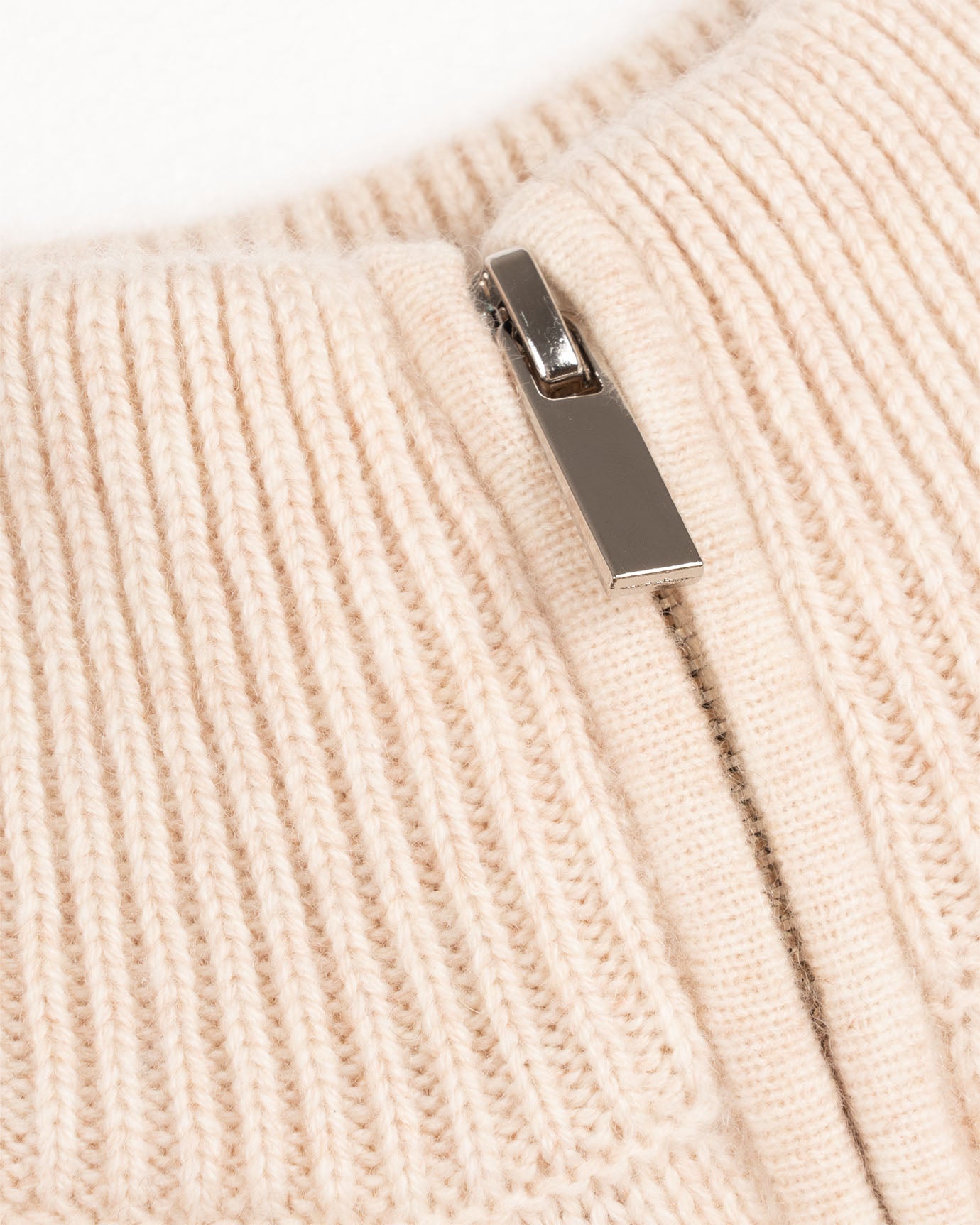 Close-up of a beige knitted fabric with a metal zipper tab.