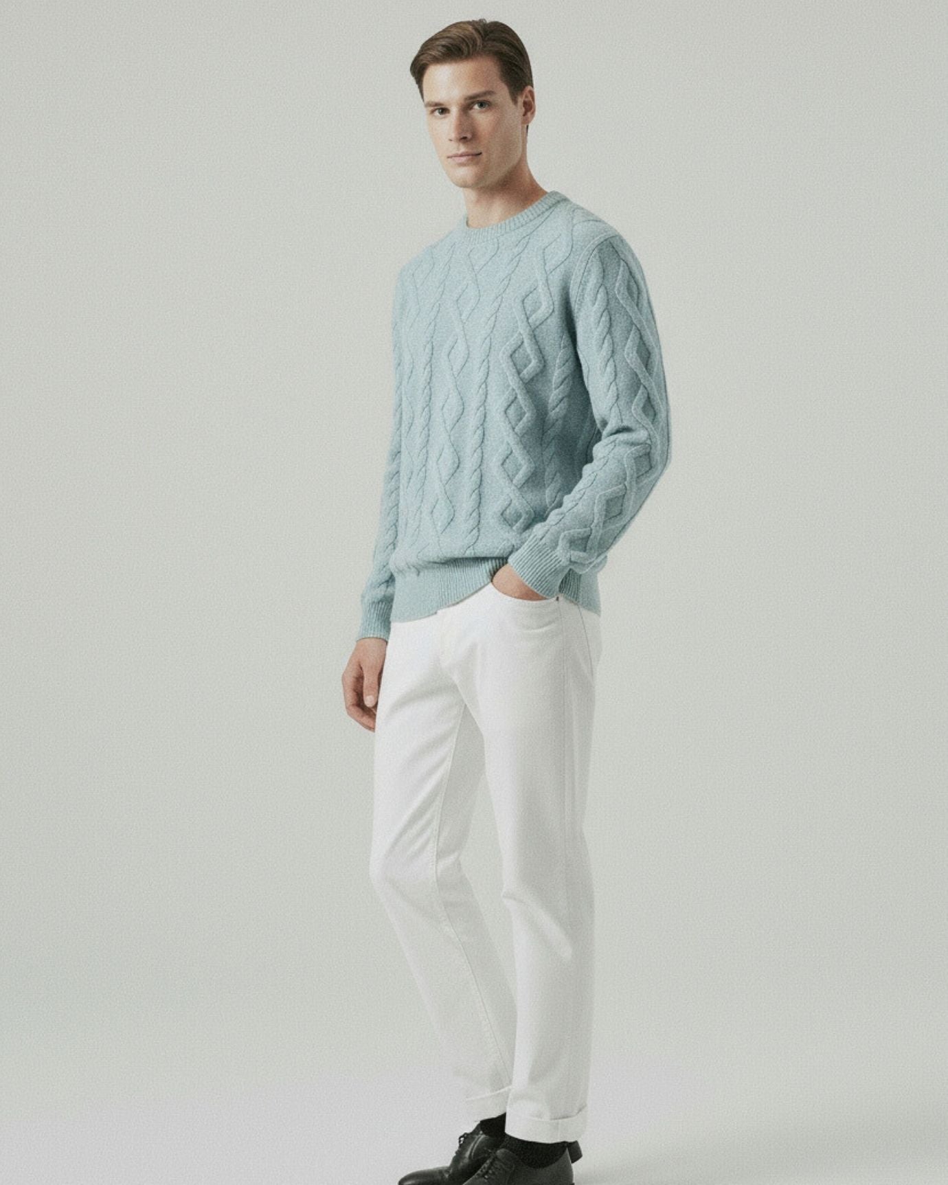 Man wearing a light blue cable knit sweater and white pants on a plain background