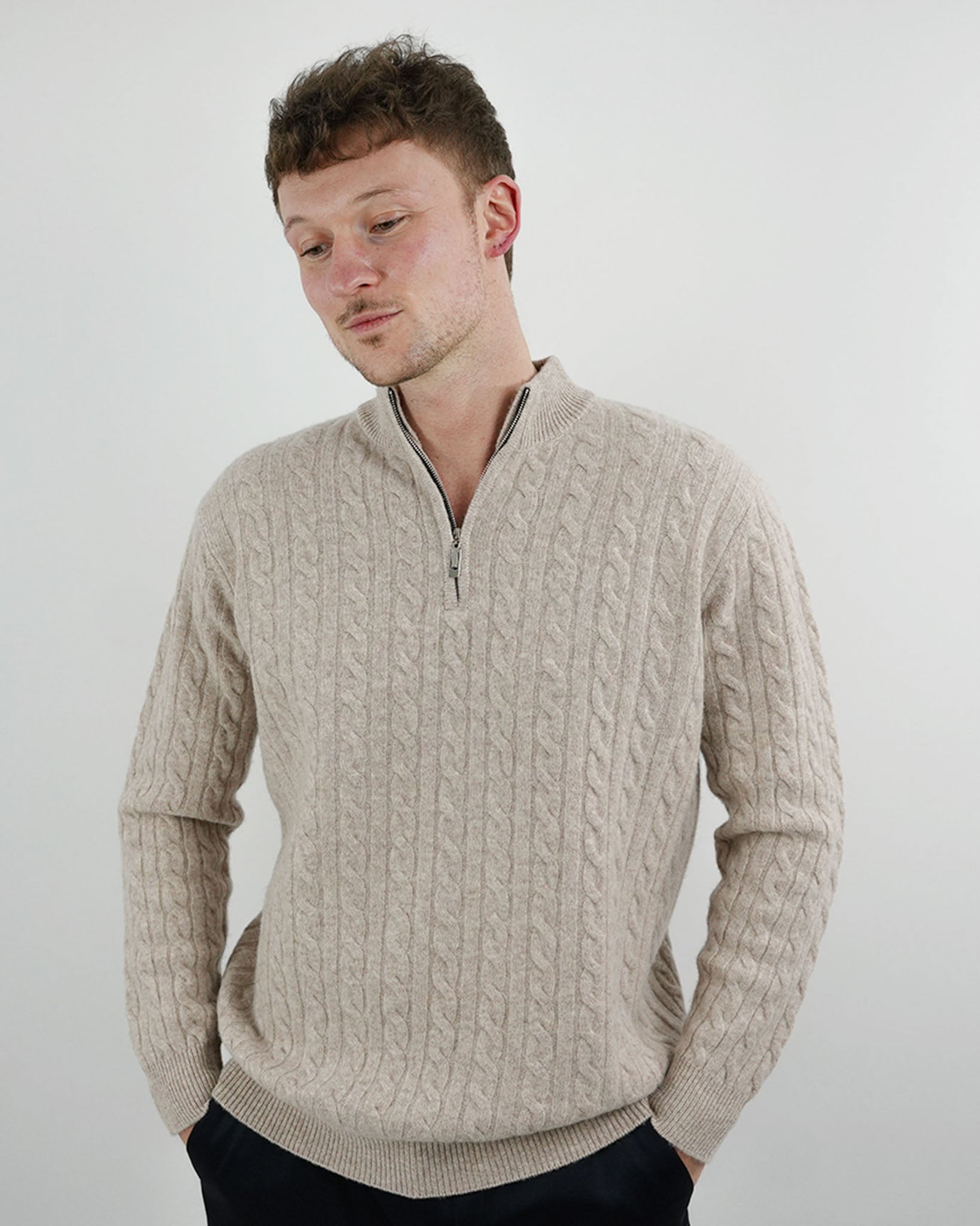 Man wearing a beige cable knit sweater with a zipper on a plain background